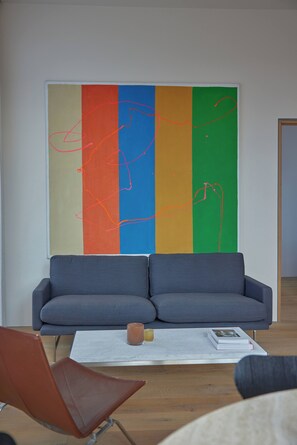 Uma sala de estar moderna com um sofá cinza, uma mesa de centro com livros e um copo, e uma pintura abstrata colorida na parede.