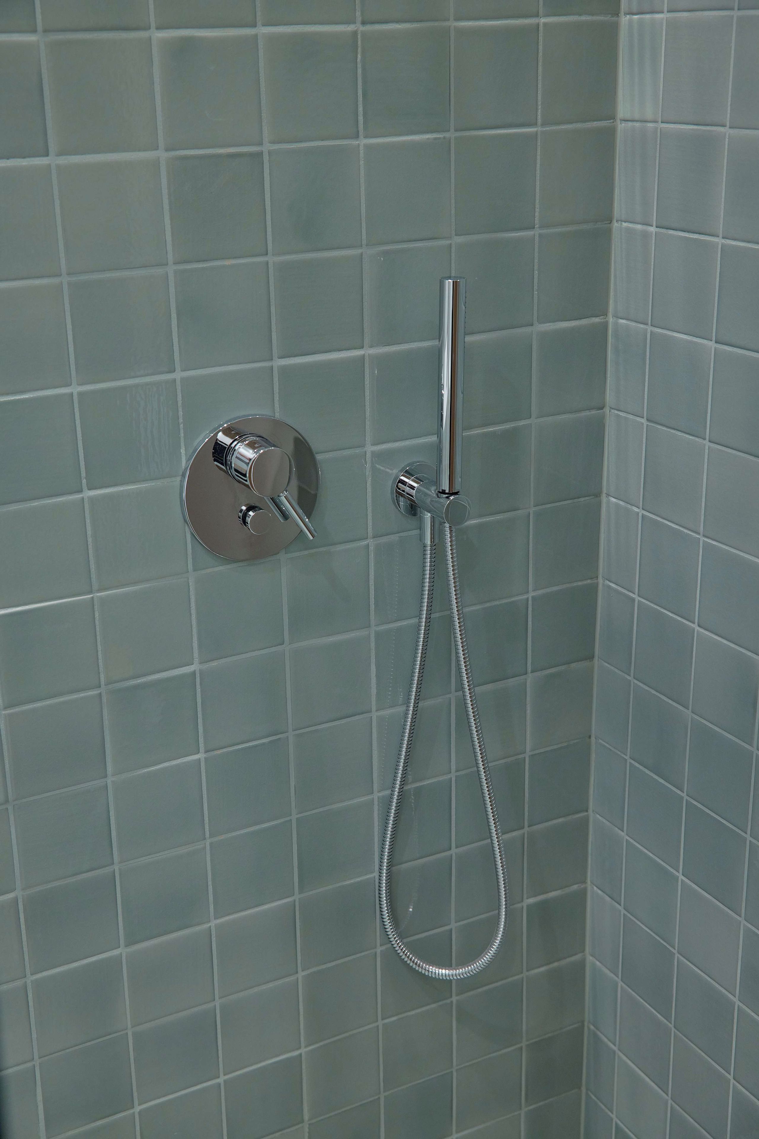A shower with a handheld showerhead and a wall-mounted control valve.