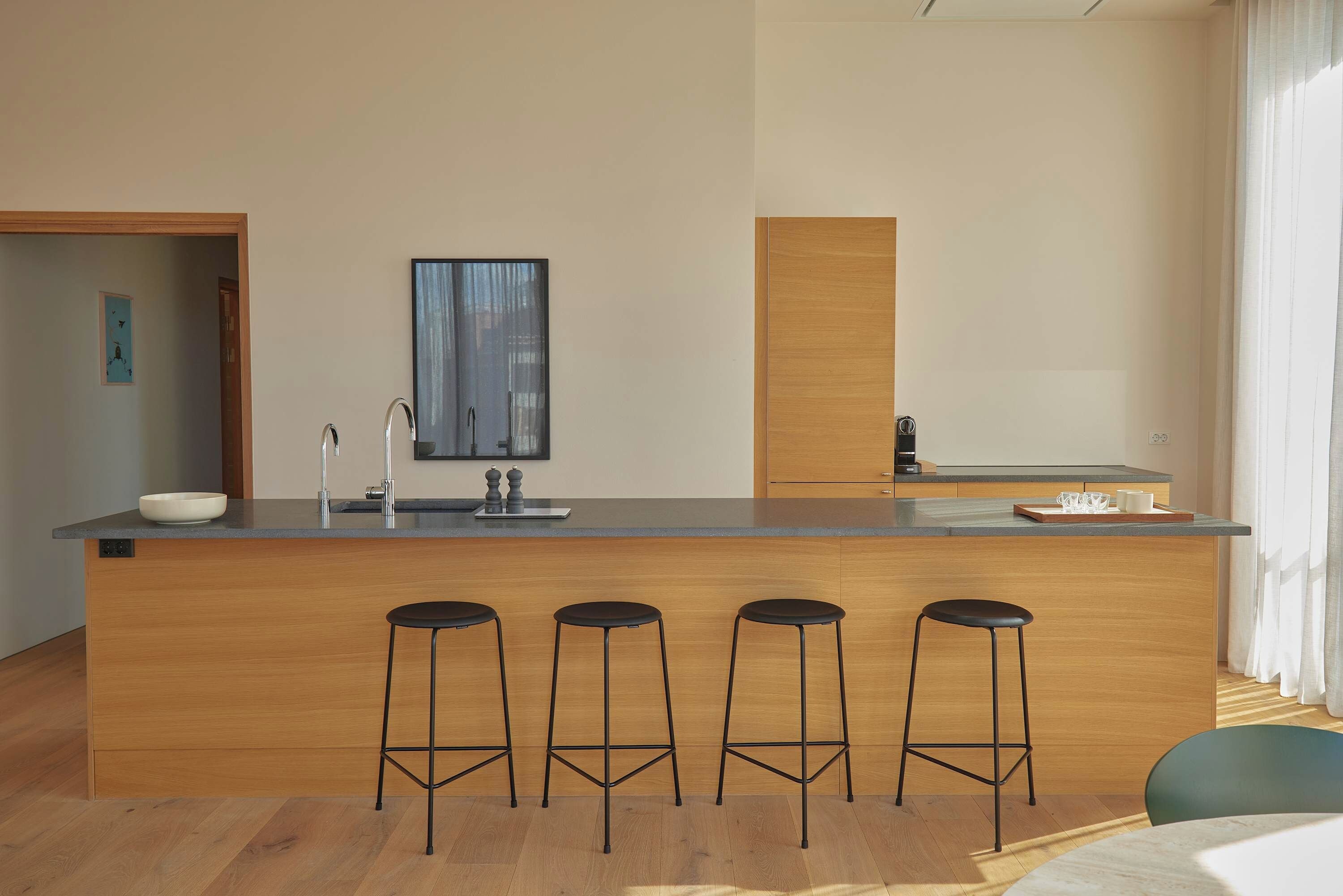 Uma cozinha moderna com uma ilha central, banquetas, máquina de café e uma janela ampla.