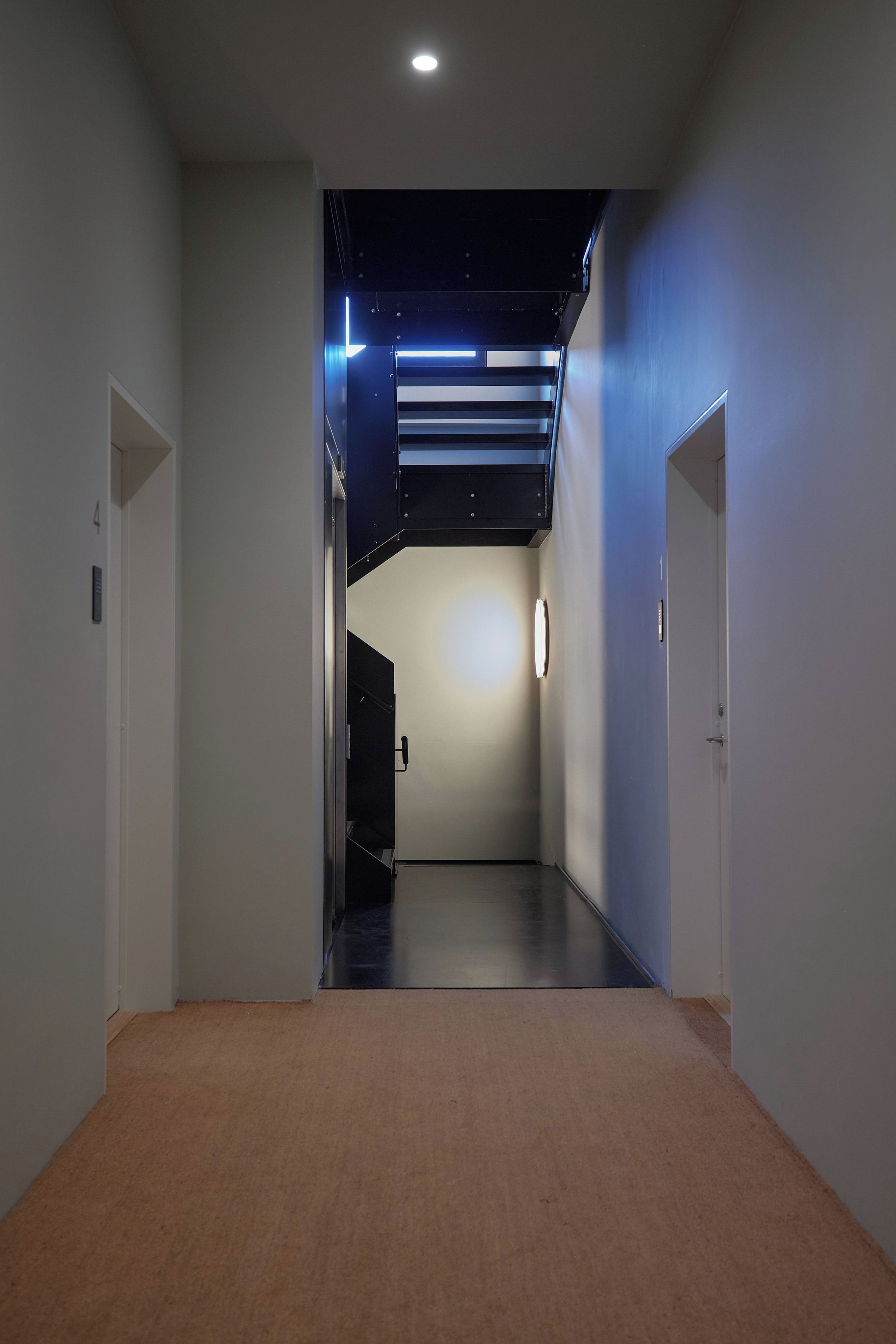 A hallway with a carpeted floor, white walls, and a ceiling with recessed lighting.