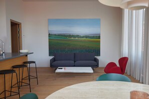Sala de estar moderna com um quadro grande de paisagem, um sofá, uma mesa de centro e um espaço bar com banquetas.