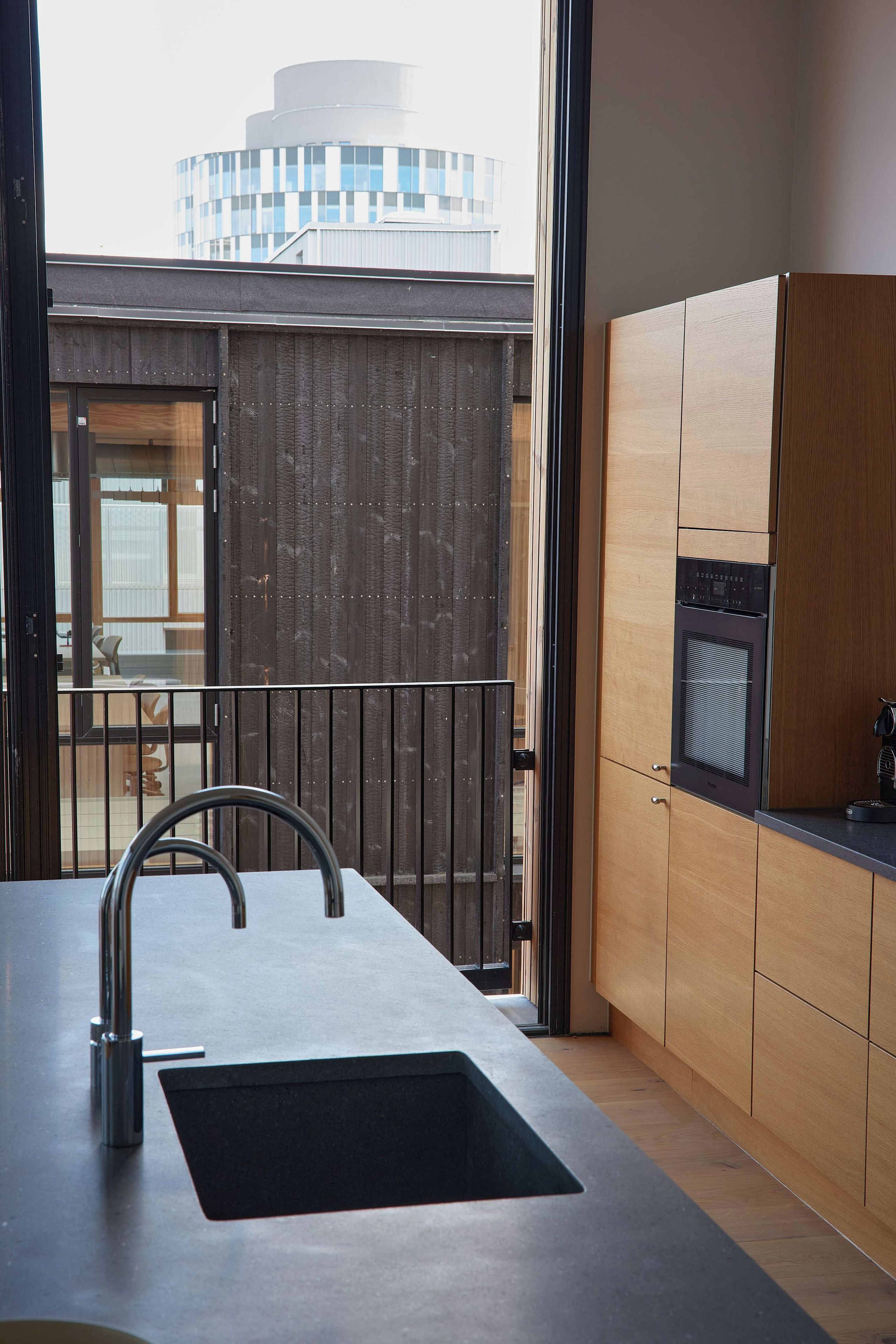 Una cocina moderna con un lavamanos grande, armarios de madera y vista a un edificio en el fondo.