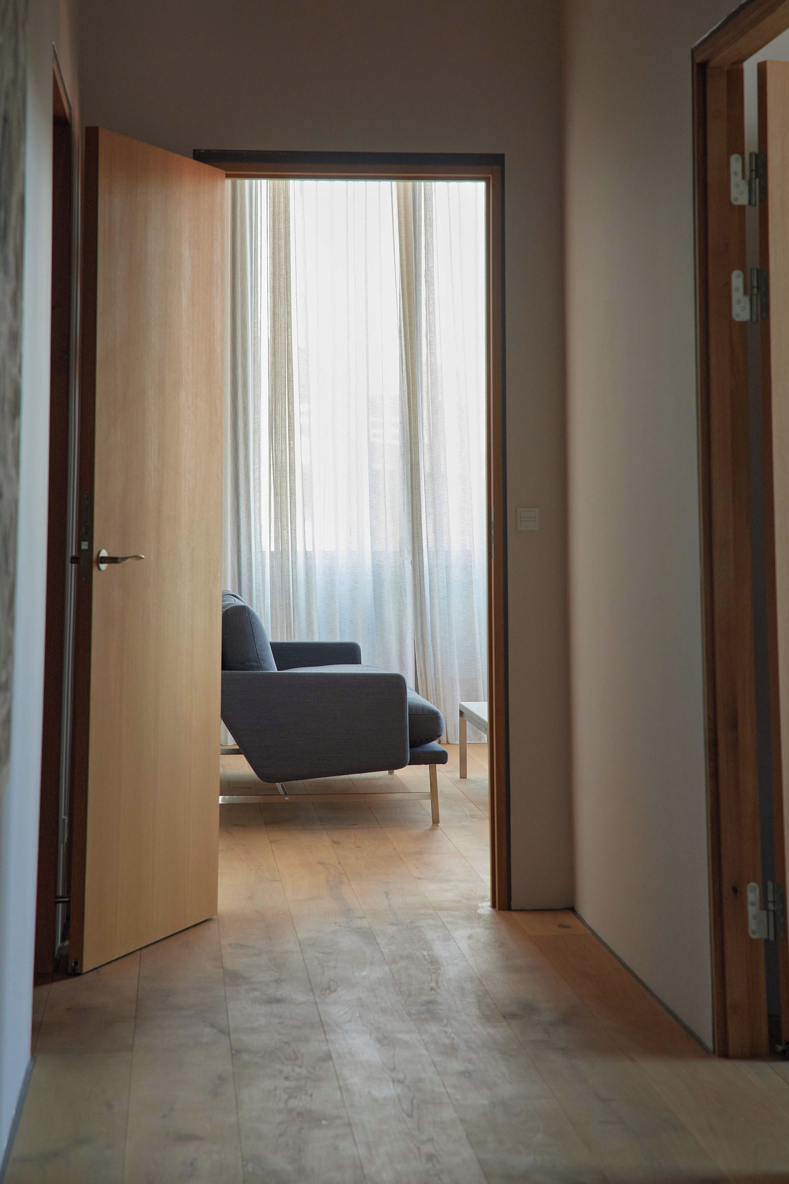 Un pasillo que conduce a un dormitorio con una cama, una silla y una ventana con cortinas.