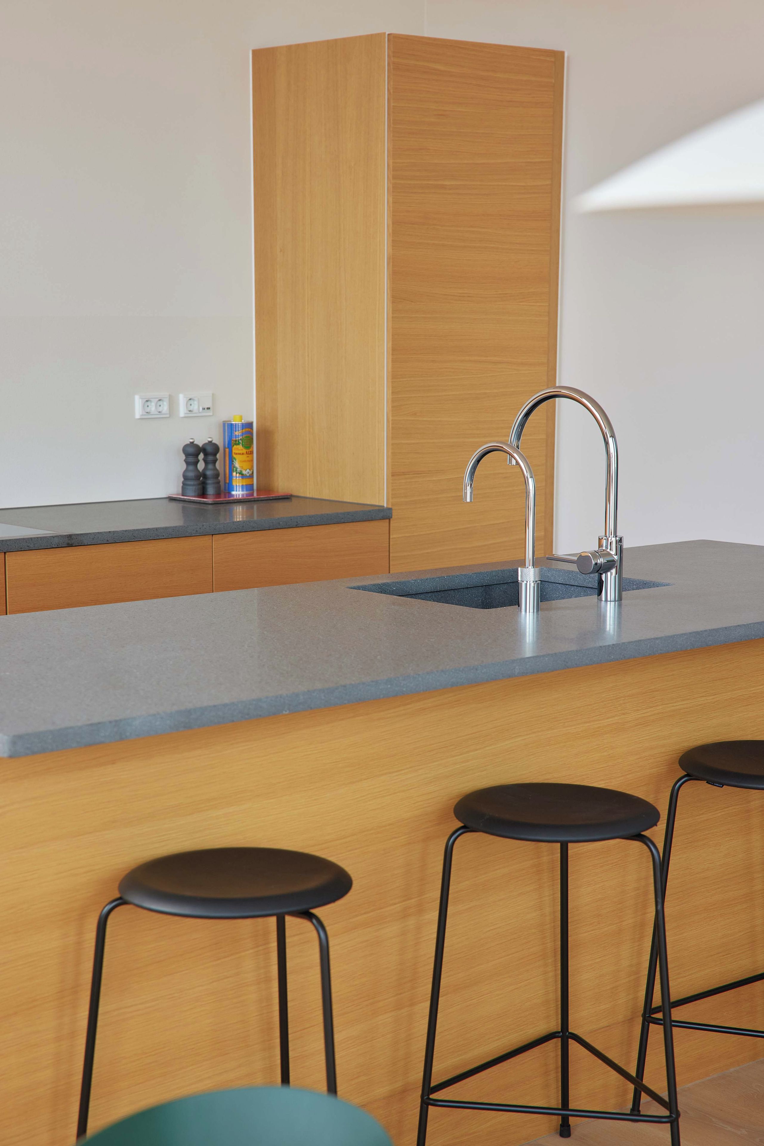 Una cocina moderna con un mueble de madera, un grifo de acero inoxidable y un taburete de bar.