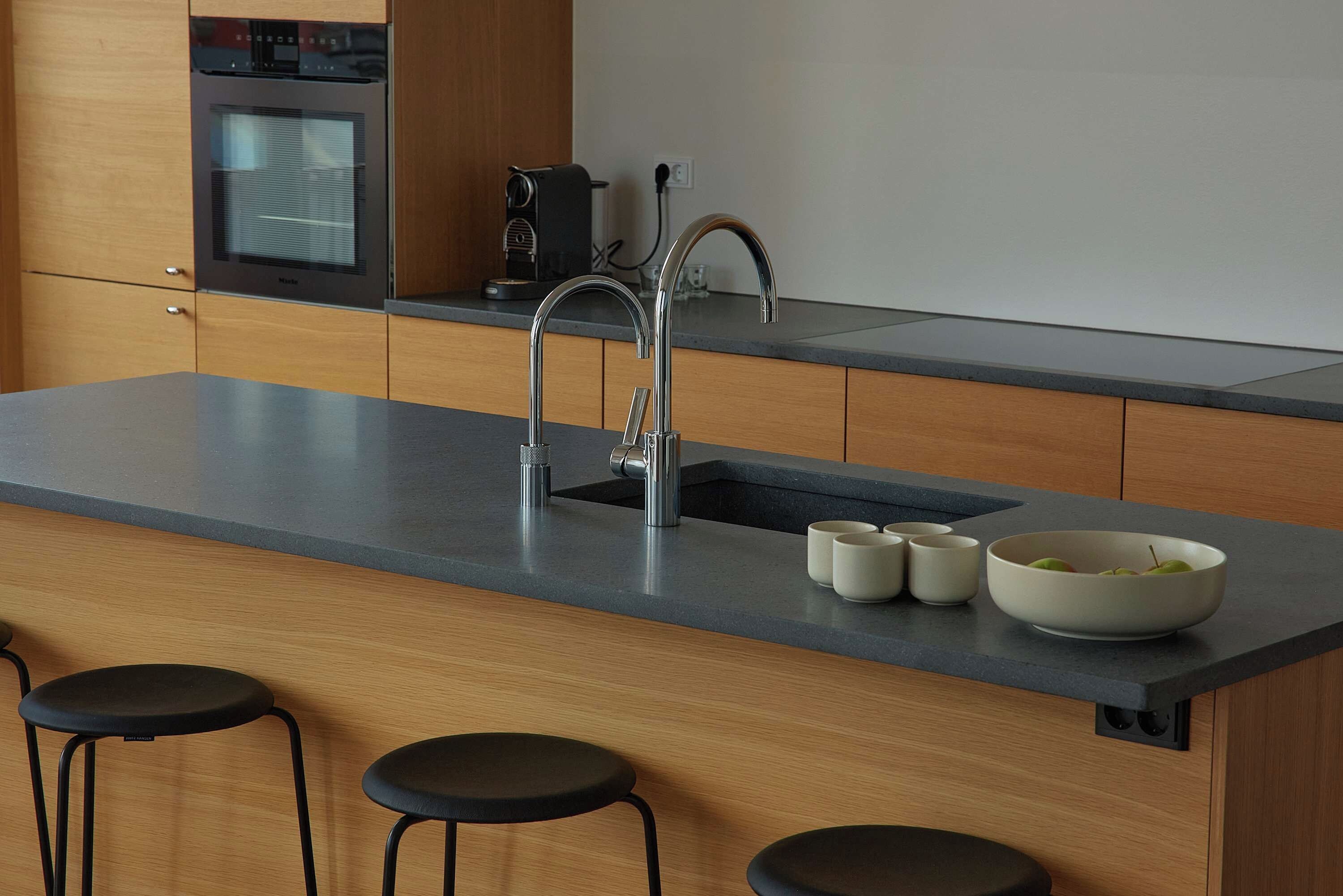 A modern kitchen with a stainless steel sink, a coffee machine, and a bowl of fruit on the counter.