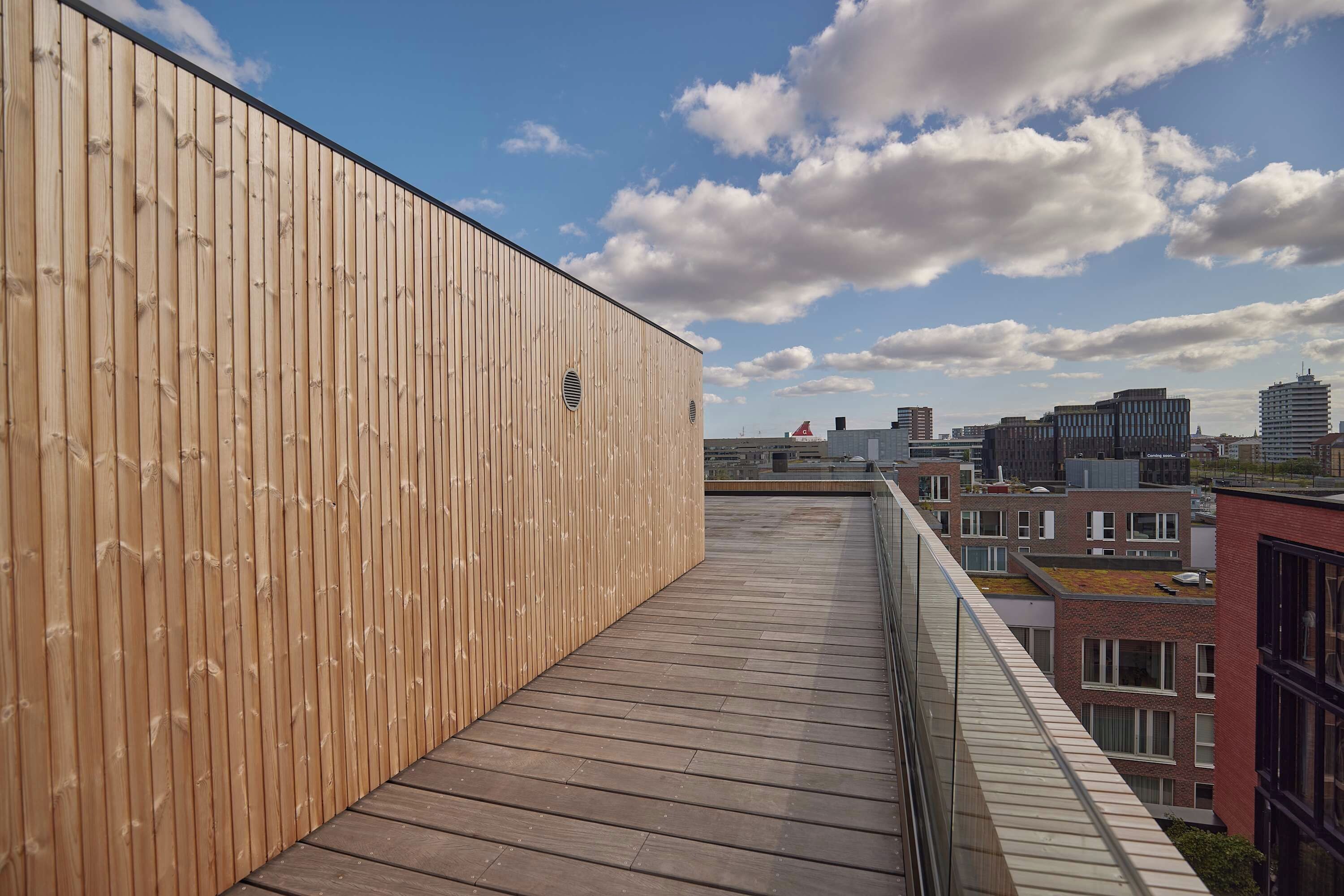 A rooftop terrace with a wooden wall and a view of the city skyline.