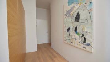 A hallway with a wooden floor, a white door, and a large abstract painting on the wall.