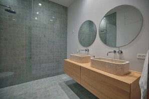 Une salle de bain moderne avec une douche à l’italienne en verre, deux vasques avec des miroirs ronds et un meuble-lavabo en bois.