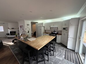 A modern kitchen with a wooden island, black bar stools, white cabinets, and a built-in oven.