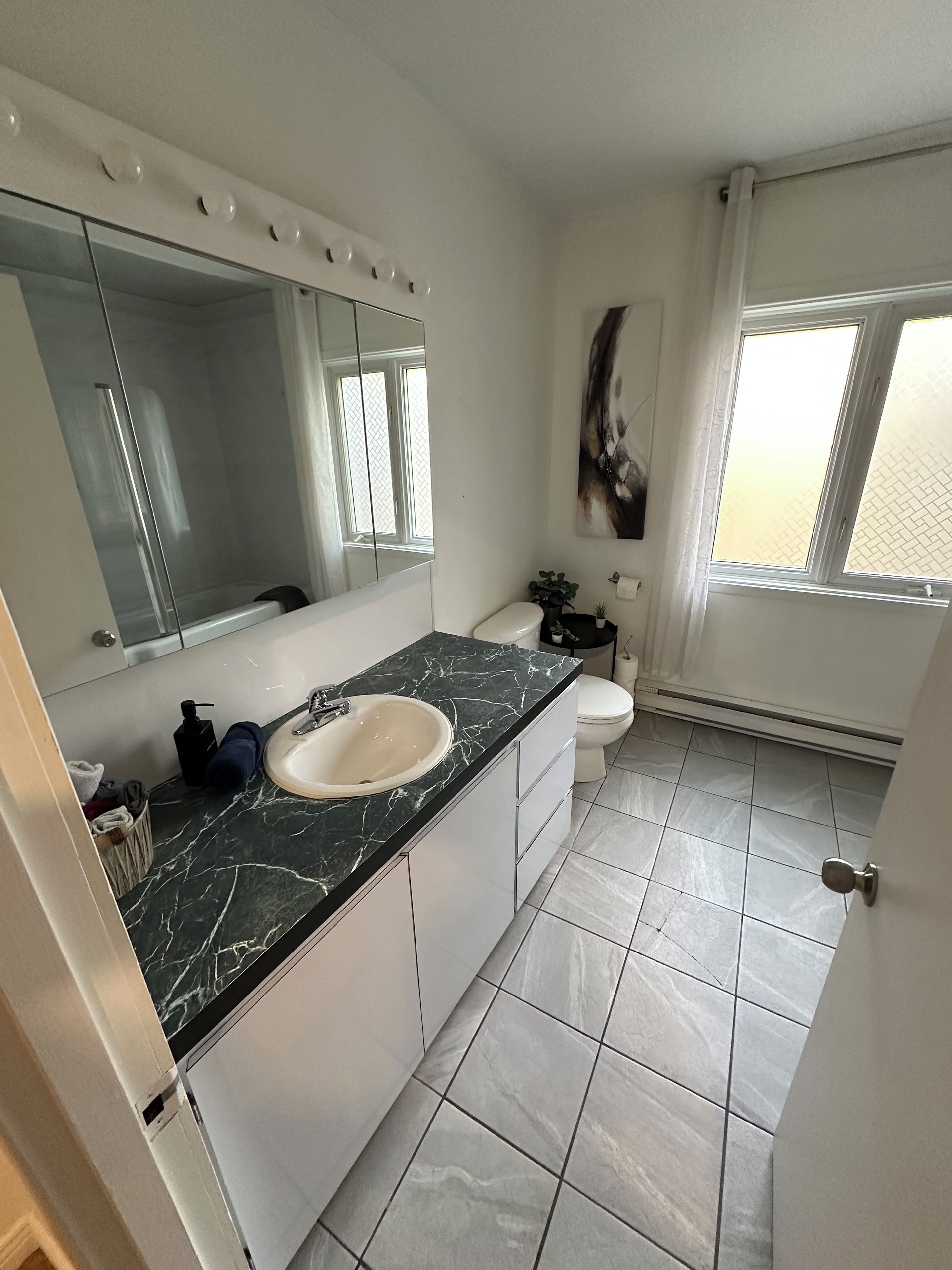 Une salle de bain avec un lavabo en marbre, des toilettes, un grand miroir et une fenêtre.