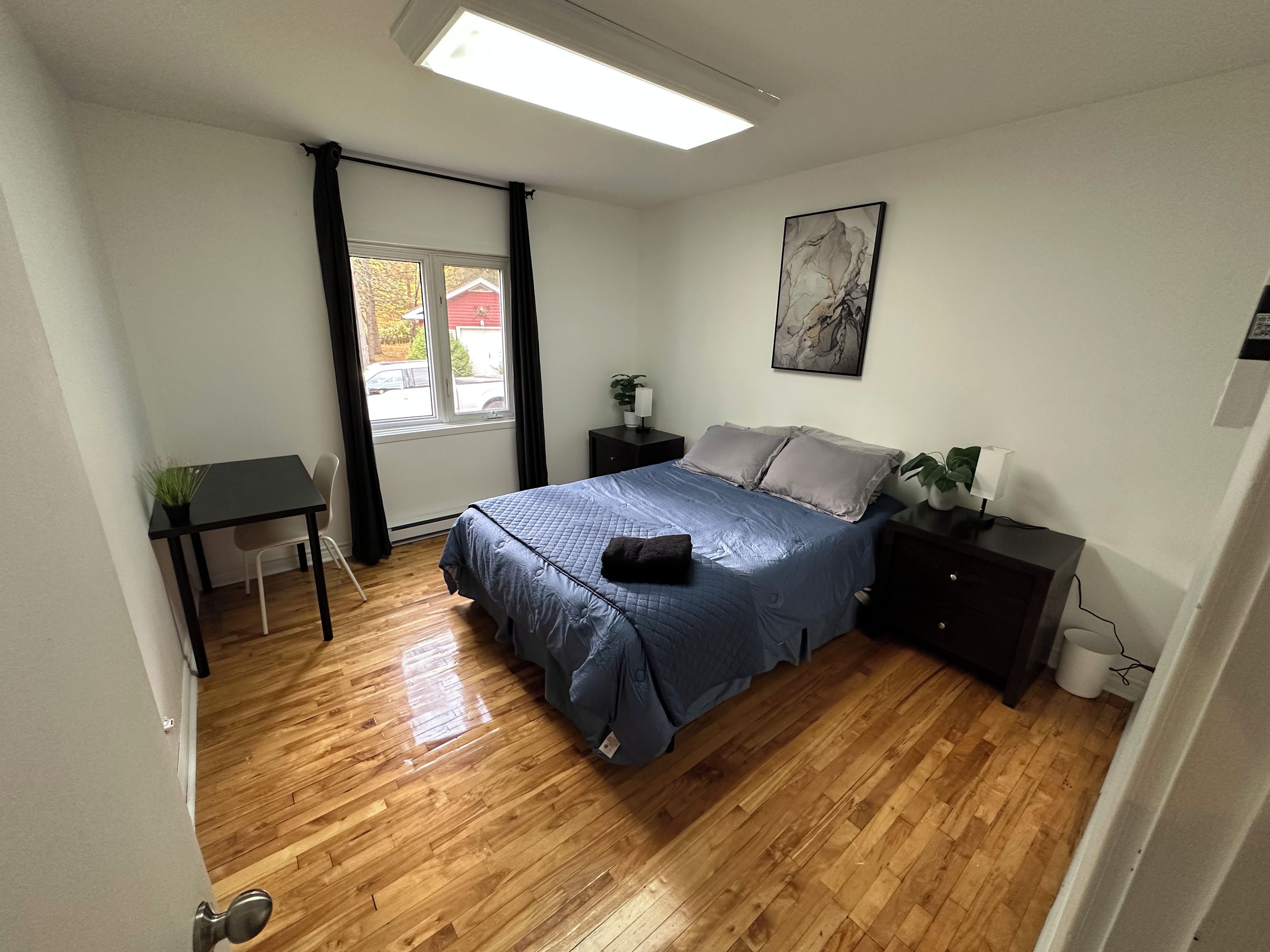 Une chambre à coucher avec un lit, des tables de chevet, un bureau et une fenêtre.