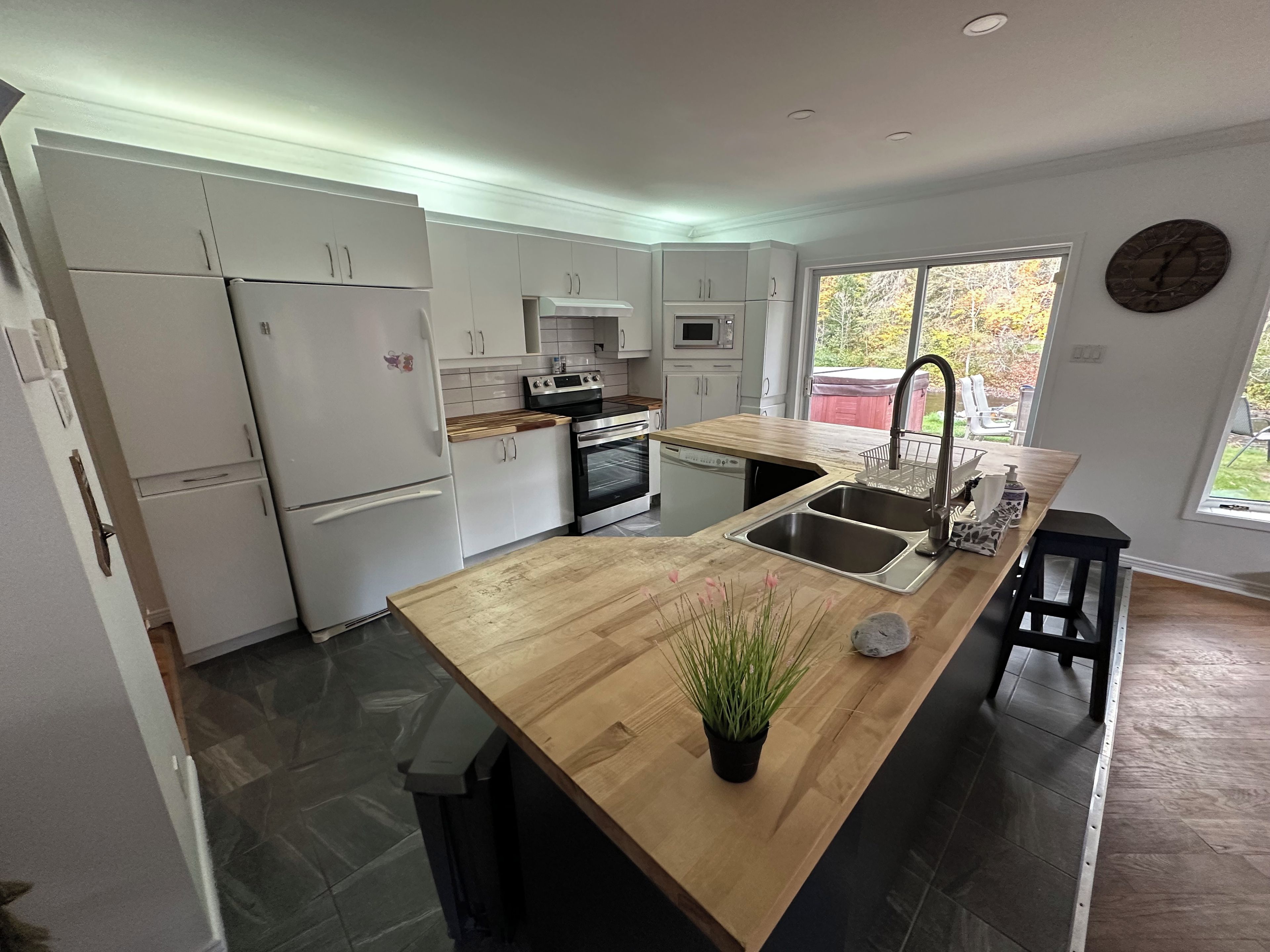 Une cuisine moderne avec des meubles blancs, un plan de travail en bois, un évier et une horloge au mur.