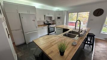 Une cuisine moderne avec des meubles blancs, un plan de travail en bois, un évier et une horloge au mur.