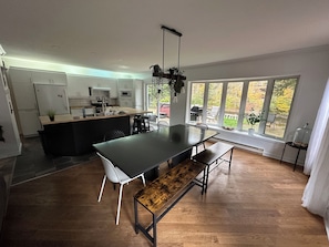 A modern kitchen with a central island, dining area with benches, and large windows offering a view of the outdoors.