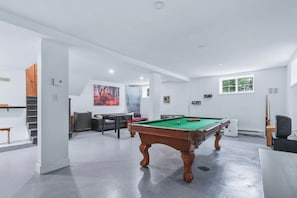 Een ruime kamer met een pooltafel, een bank en een schilderij aan de wand.