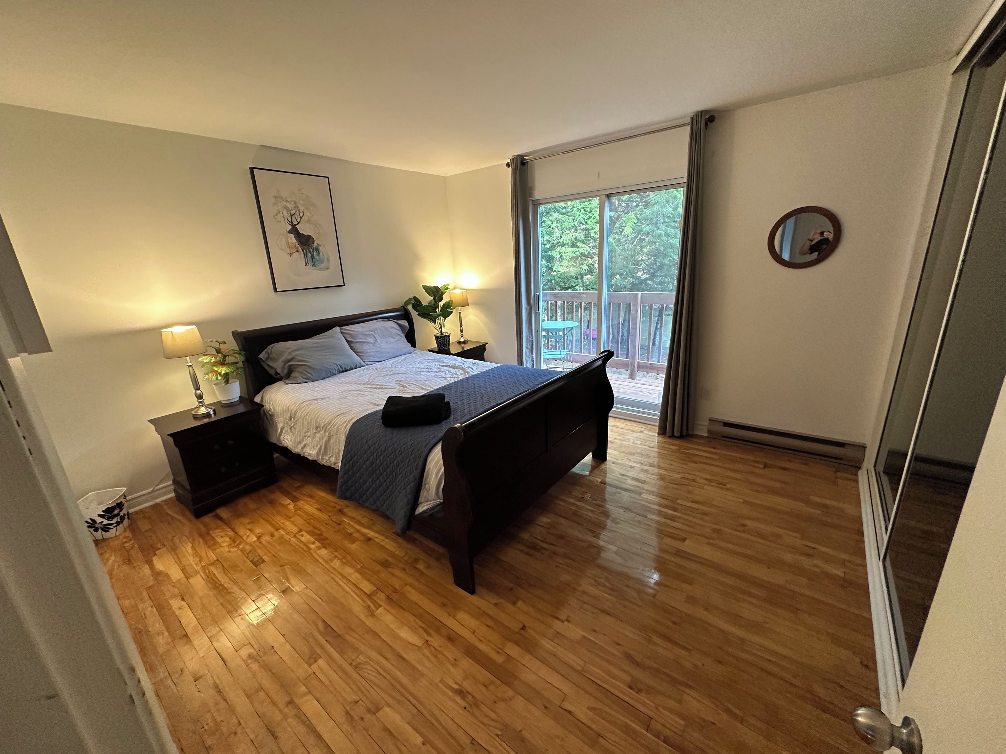 A bedroom with a bed, bedside tables, a nightstand, a potted plant, and a view of a balcony.