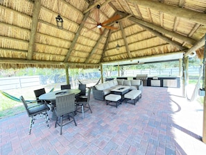 An outdoor patio with a thatched roof, wicker furniture, and a grill area.