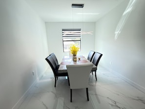 A dining area with a marble-tiled floor, a rectangular table with chairs, a hanging light fixture, and a window with a view.