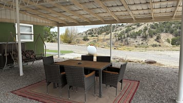 En udendørs terrasse med bord og stole, en gyngestativ og udsigt over et bakket landskab.