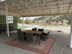 Eine Terrasse im Freien mit Tisch und Stühlen, einer Schaukel und Blick auf eine hügelige Landschaft.