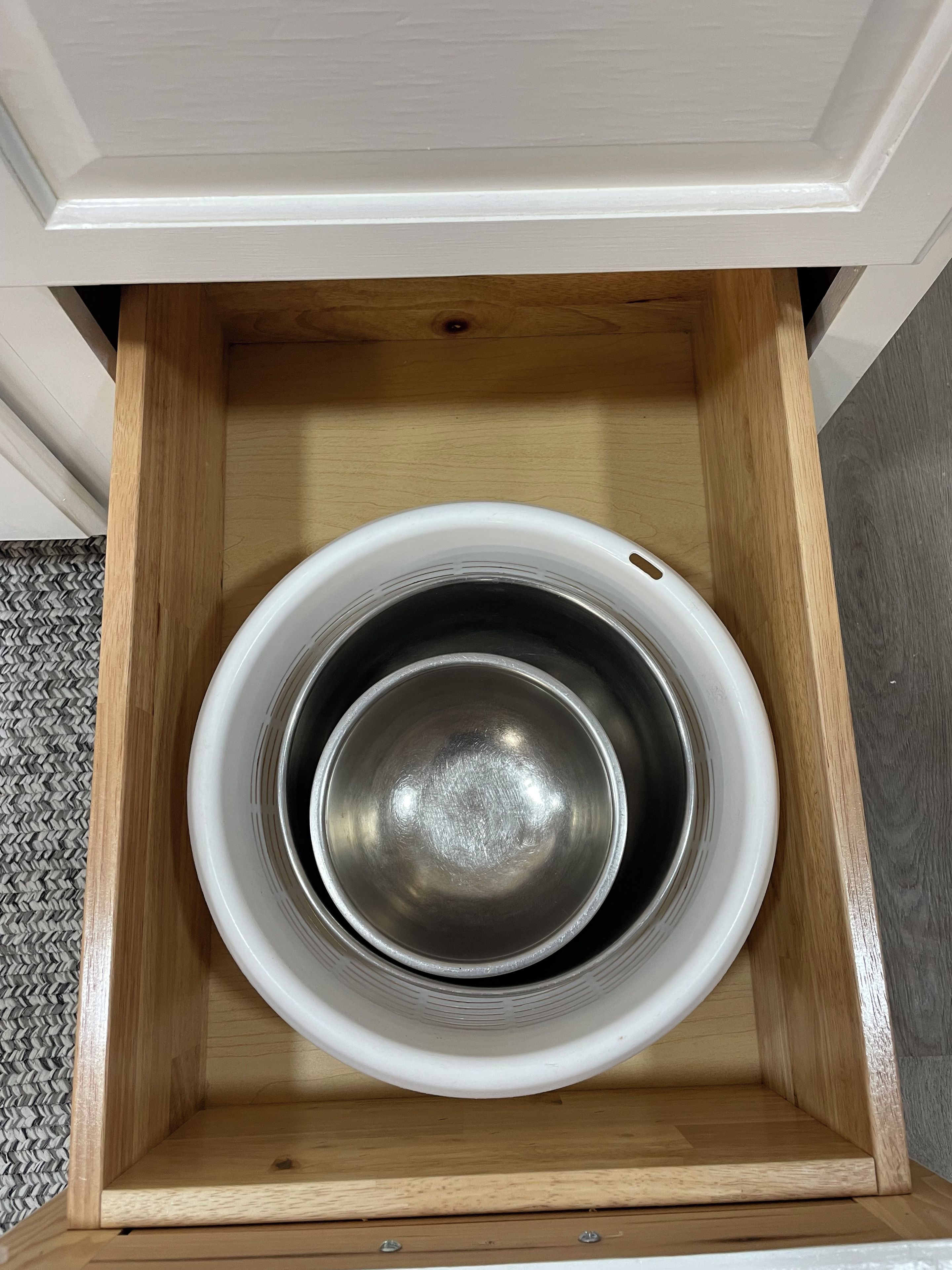 Uma tigela de metal branca dentro de uma gaveta de madeira.