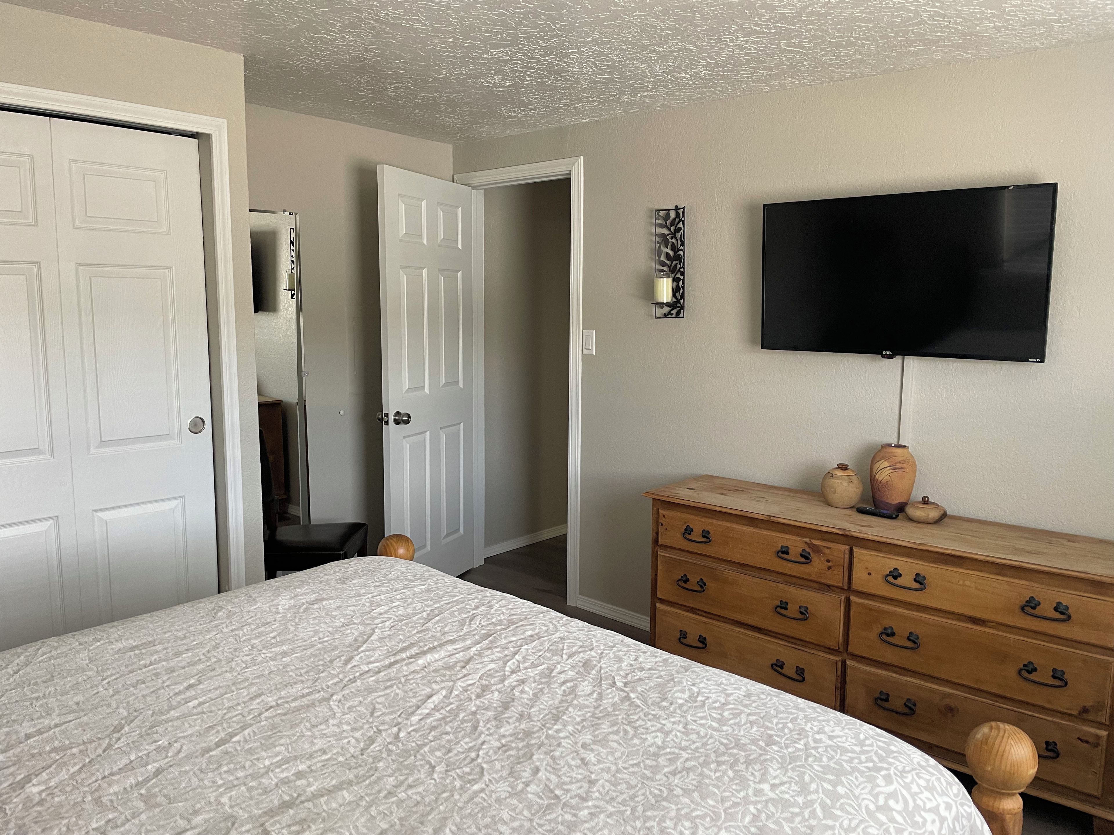 Quarto com cama, penteadeira, televisão e porta que dá para outro cômodo.