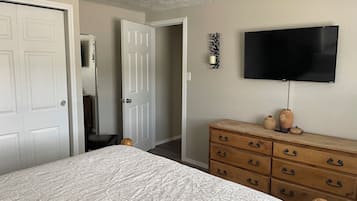 Quarto com cama, penteadeira, televisão e porta que dá para outro cômodo.
