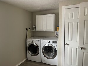 A laundry room with two front-loading washing machines, a white door, and a shelf above the machines.