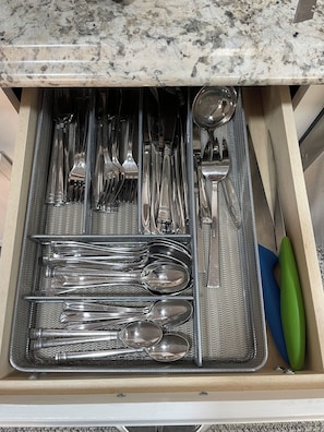 Un cajón con diversos utensilios de cocina, incluyendo cucharas, tenedores, cuchillos y una espátula.