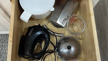 A drawer containing kitchen utensils including a grater, measuring cups, and a whisk.
