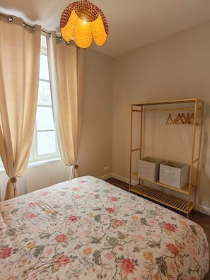 A bedroom with a bed, curtains, a hanging light fixture, and a wardrobe with hangers. - Suite Adélaïde, Élégance Rétro au cœur de la ville (Landerneau)