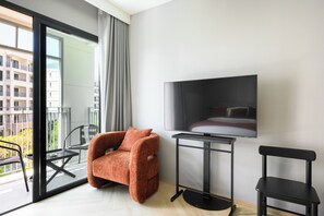A modern hotel room with a sofa, a TV mounted on the wall, a small table, and a chair. - Bang Tao - Scenic Pool Views (Tambon Choeng Thale)