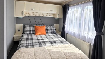 Un dormitorio con cama, mesita de noche, armario y ventana con cortinas.