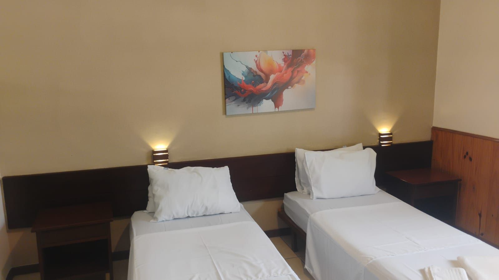 Una habitación de hotel con dos camas individuales, una mesita de noche con lámpara y un armario de madera.