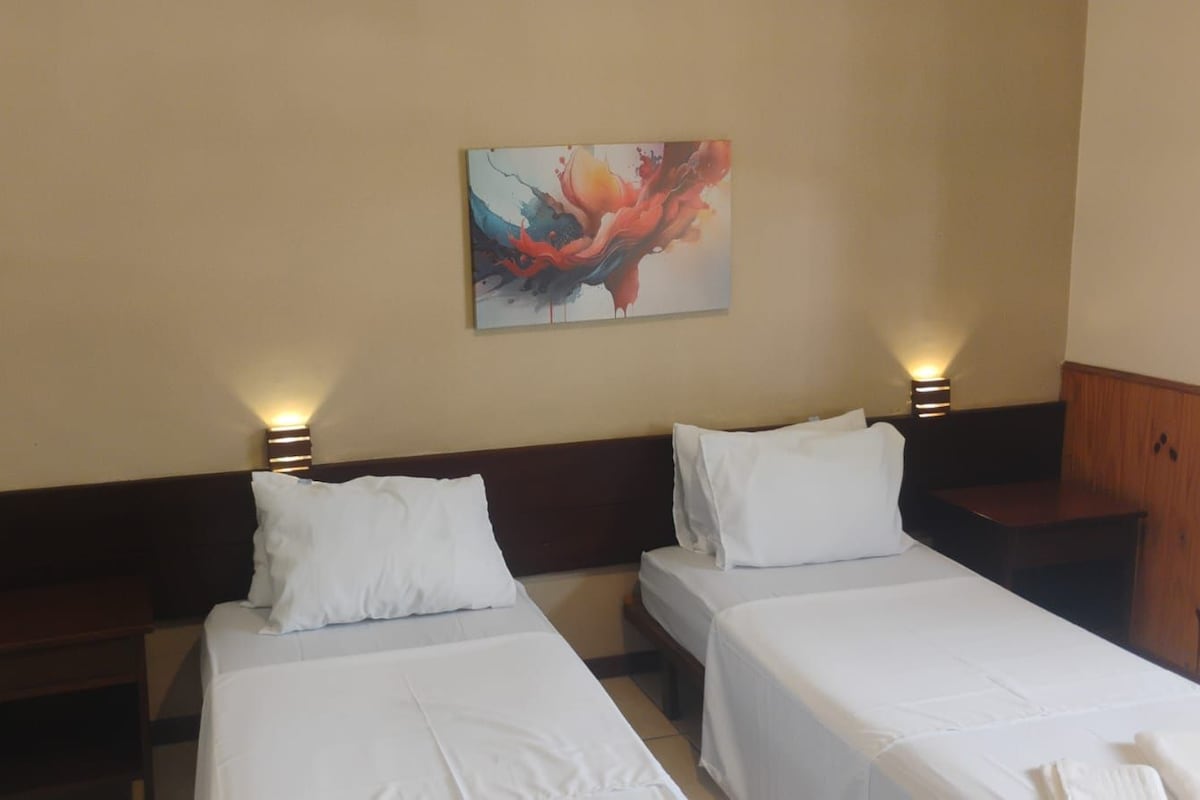 Ein Hotelzimmer mit zwei Einzelbetten, einem Nachttisch mit Lampe und einem Holzschrank.