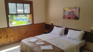A hotel room with a bed, a window with a view of greenery, and a painting on the wall.