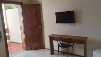 Ett rum med ett skrivbord i trä, en svart stol, en tv som är monterad på väggen och en dörr i trä.