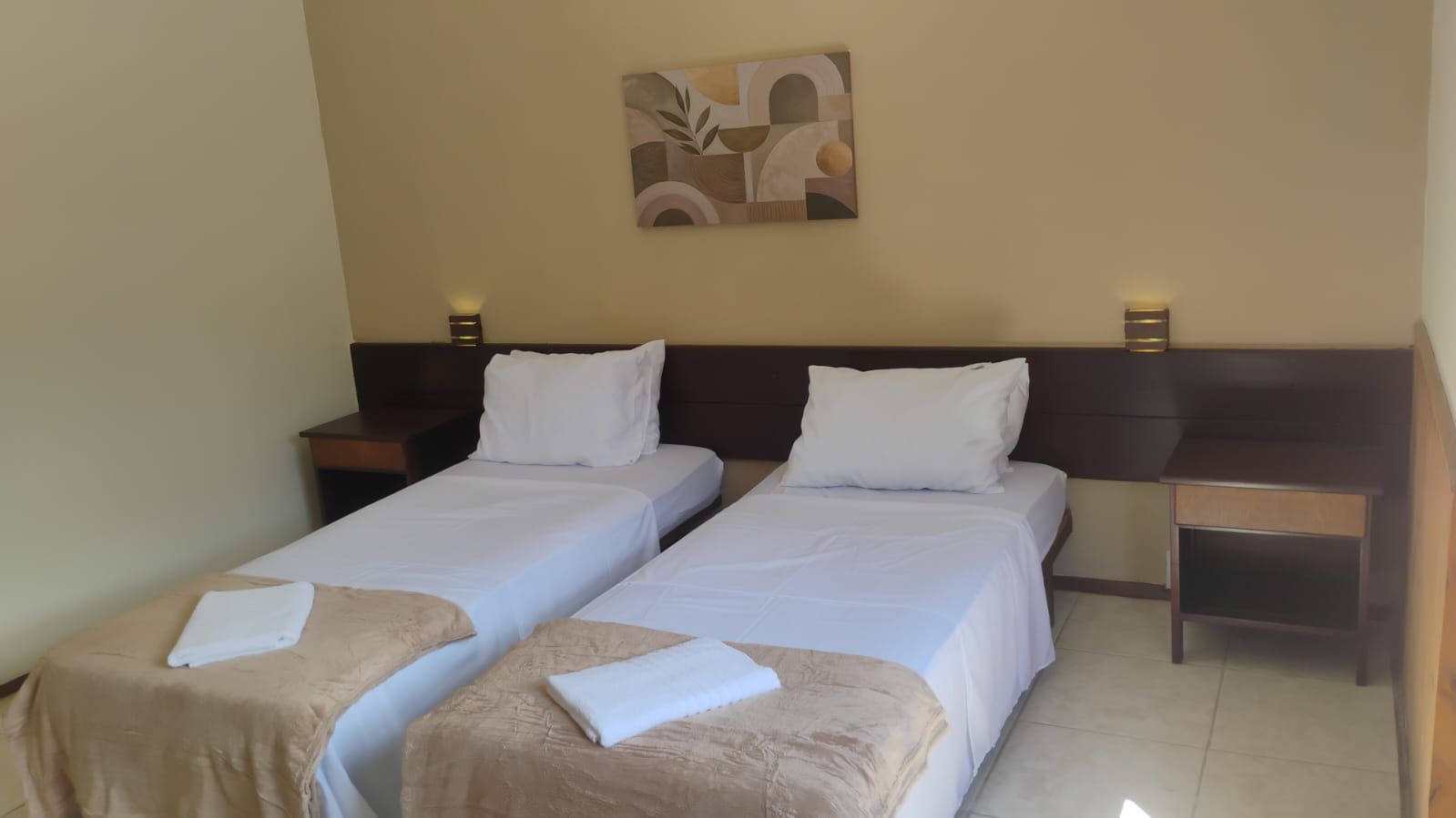 Habitación de hotel con dos camas individuales, cabeceras, mesitas de noche y una obra de arte colgada en la pared.