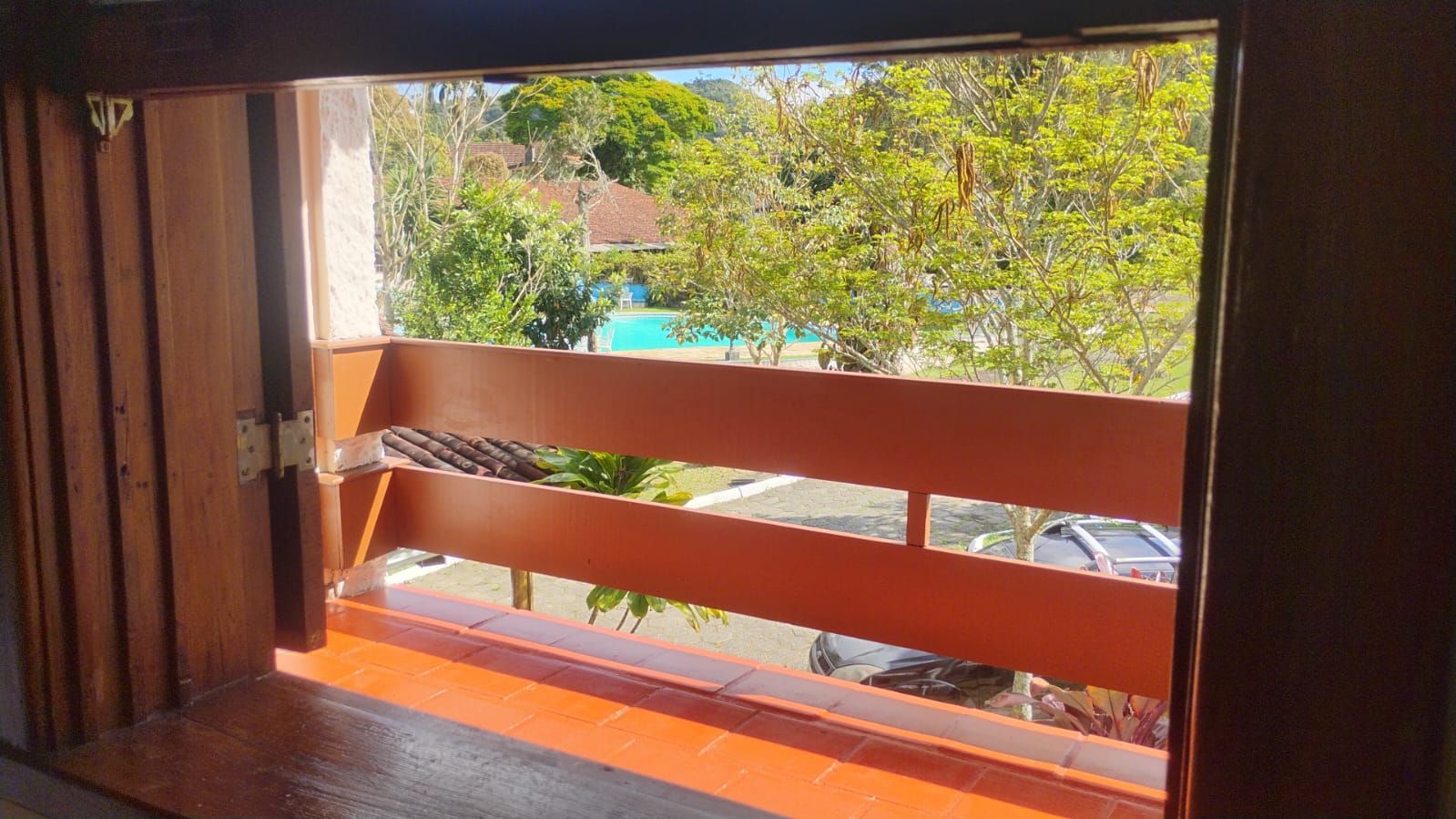 Un balcón con vista a una piscina y coches aparcados.