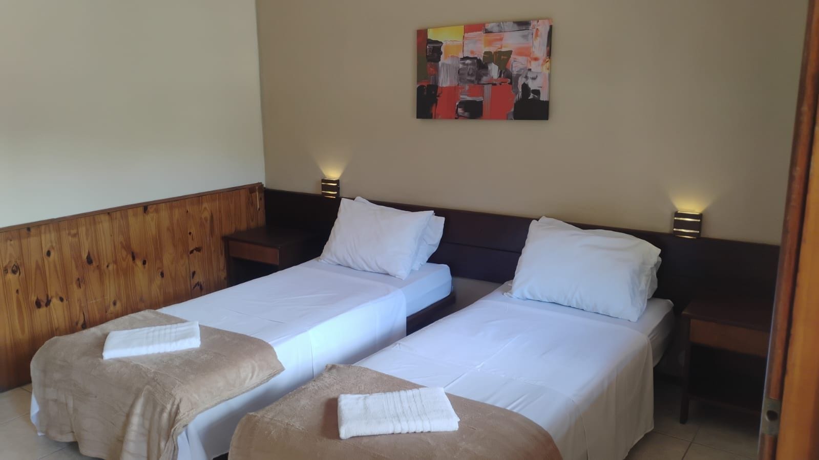 Una habitación de hotel con dos camas individuales, cabecero de madera, mesitas de noche y un cuadro en la pared.