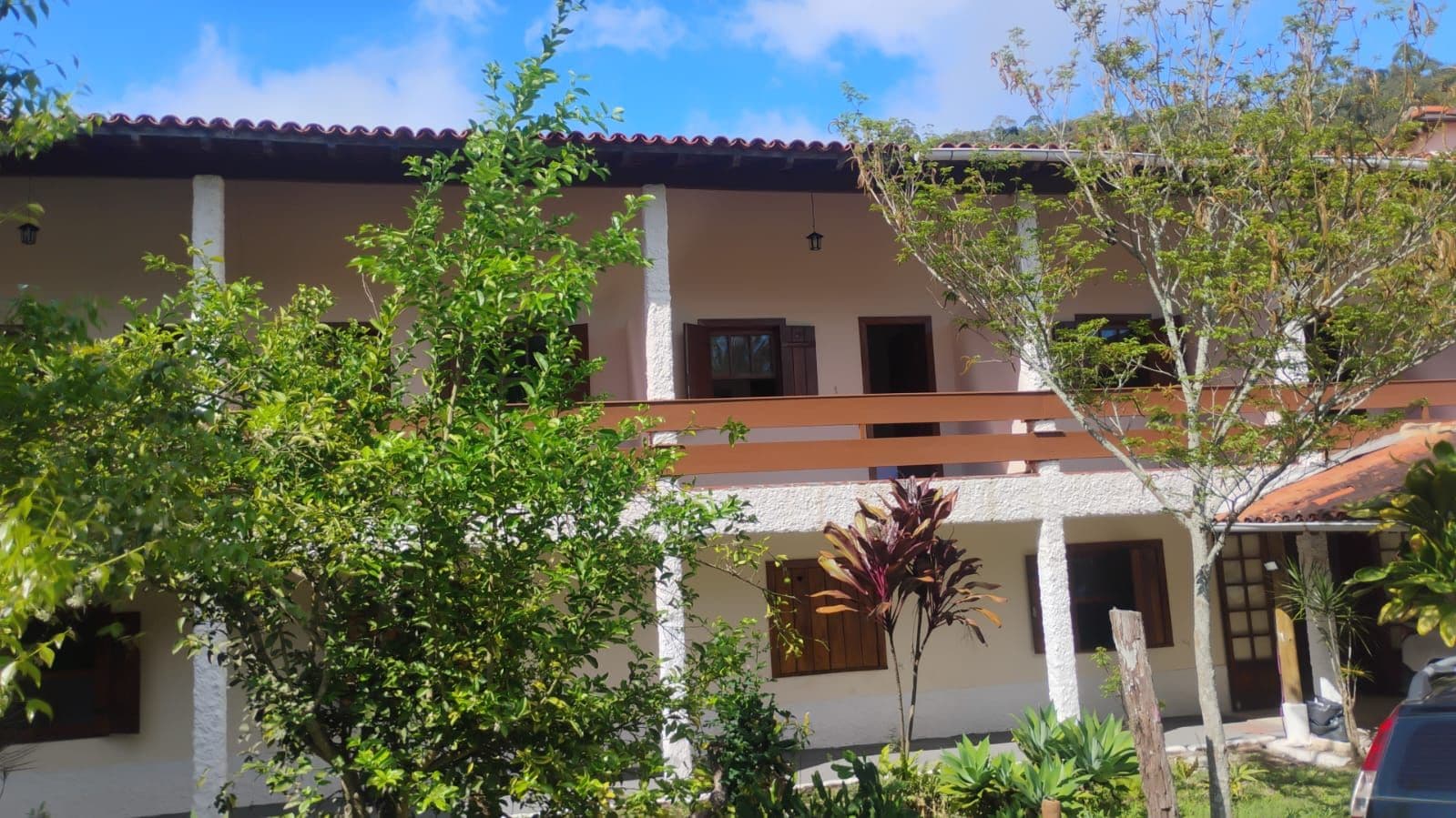A two-story building with a balcony, surrounded by greenery and a clear sky.