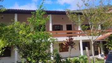 A two-story building with a balcony, surrounded by greenery and a clear sky.