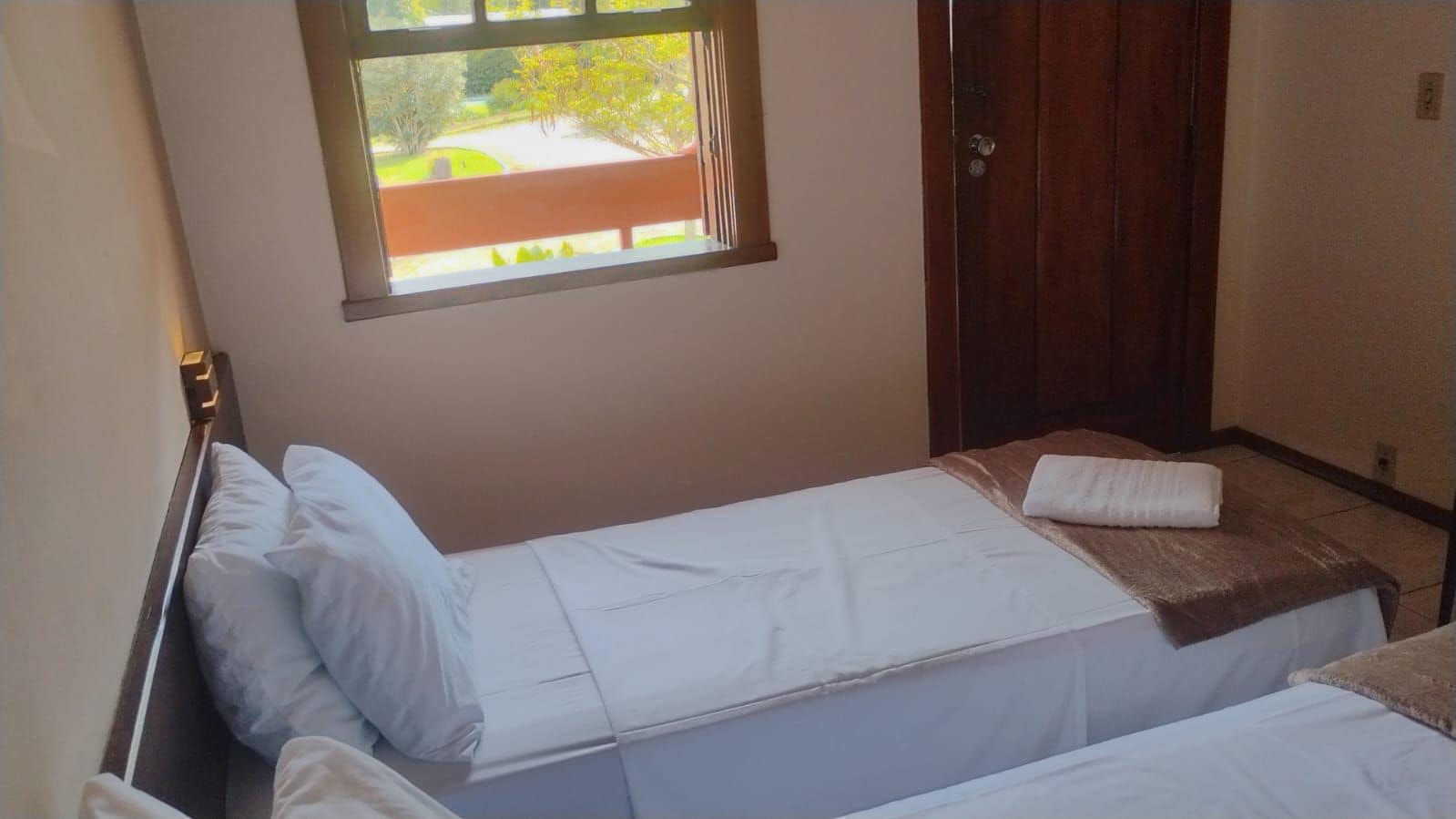 A small, single-bed room with a window, a door, and a bench.