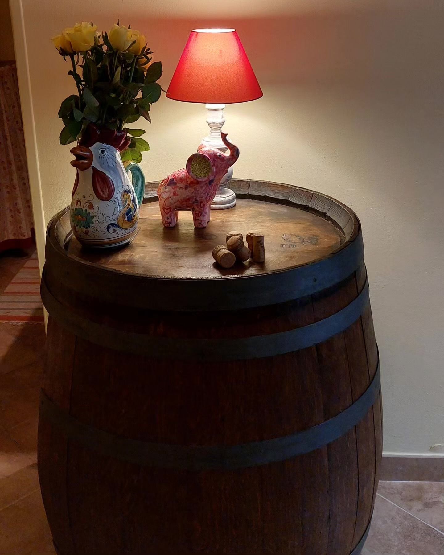Una botte di legno usata come tavolo, con un vaso di fiori e un salvadanaio sopra.
