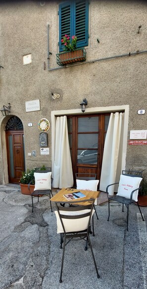 Un'area esterna con posti a sedere, un tavolo, sedie, una porta in legno e una finestra con tende.