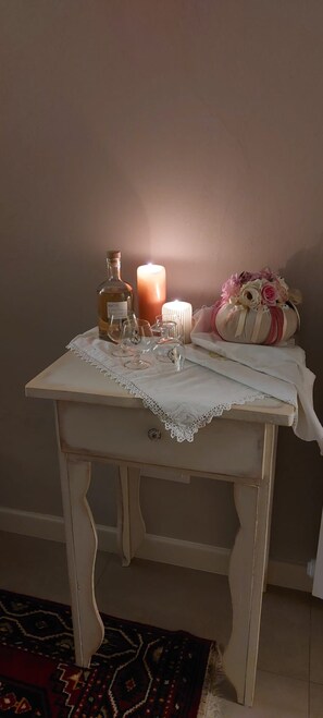 Una pequeña mesa blanca con mantel de encaje, una vela, una botella y un objeto decorativo.