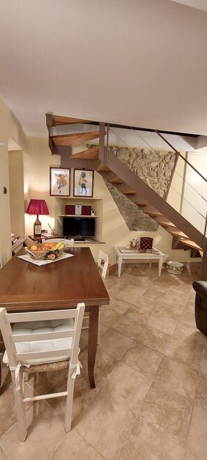 Un comedor con una mesa de madera, sillas, un televisor y una pared de piedra.
