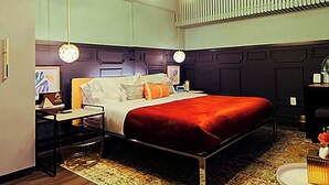 Et hotelværelse med seng, sengeborde, et skrivebord og en stol. Der er ventilator i loftet og en radiator på væggen.