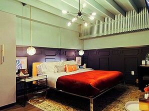 A hotel room with a bed, bedside tables, a desk, and a chair. There is a ceiling fan and a wall-mounted radiator. - Wilton Manors King Suite Walk to the Drive - North (Wilton Manors)