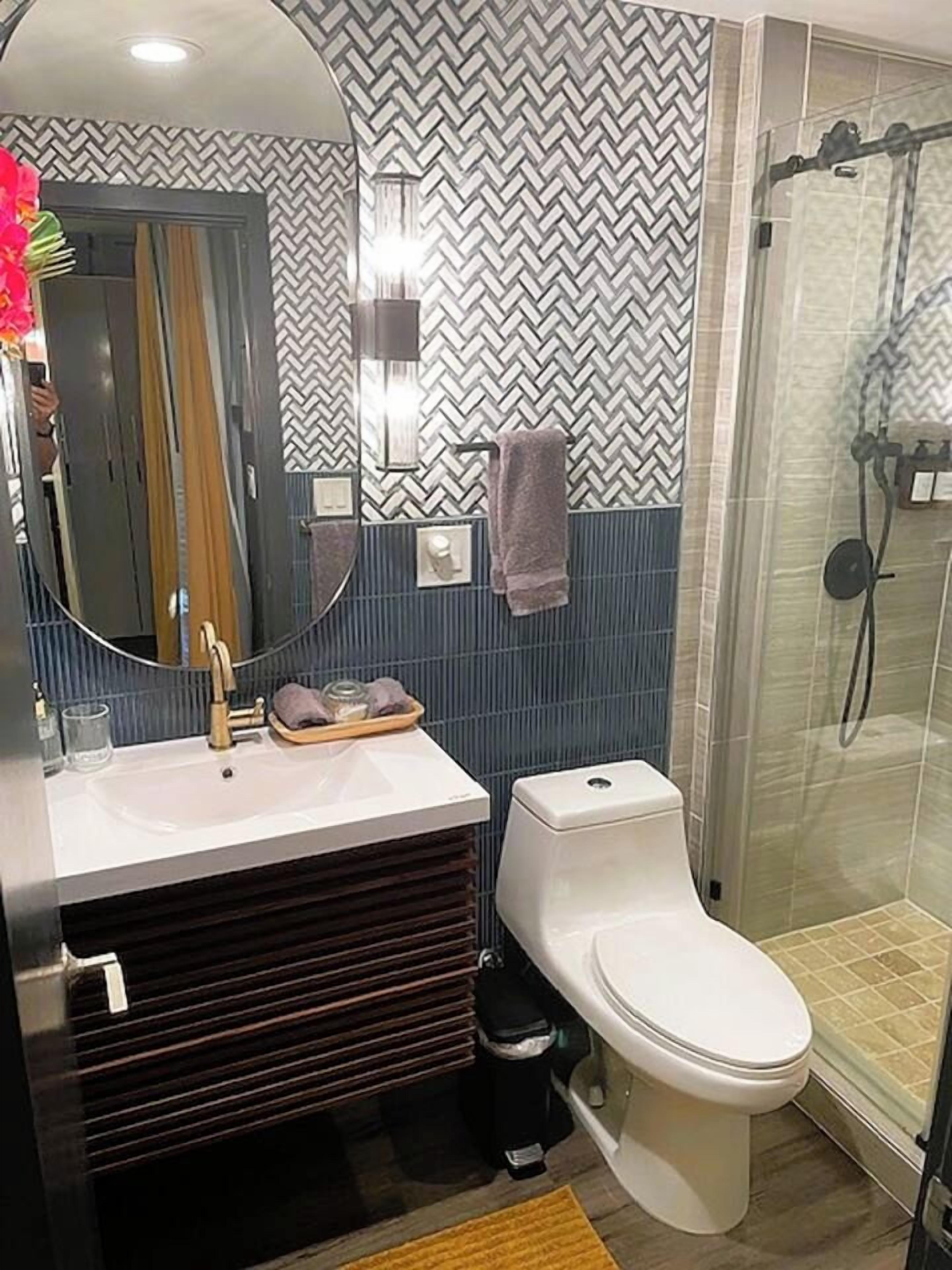Un baño con diseño moderno, que cuenta con un espejo, lavabo, inodoro y ducha.